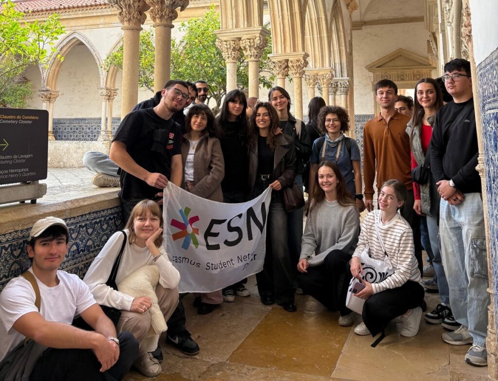Студенти з банером ESN у галереї старовинного монастиря з готичними арками.