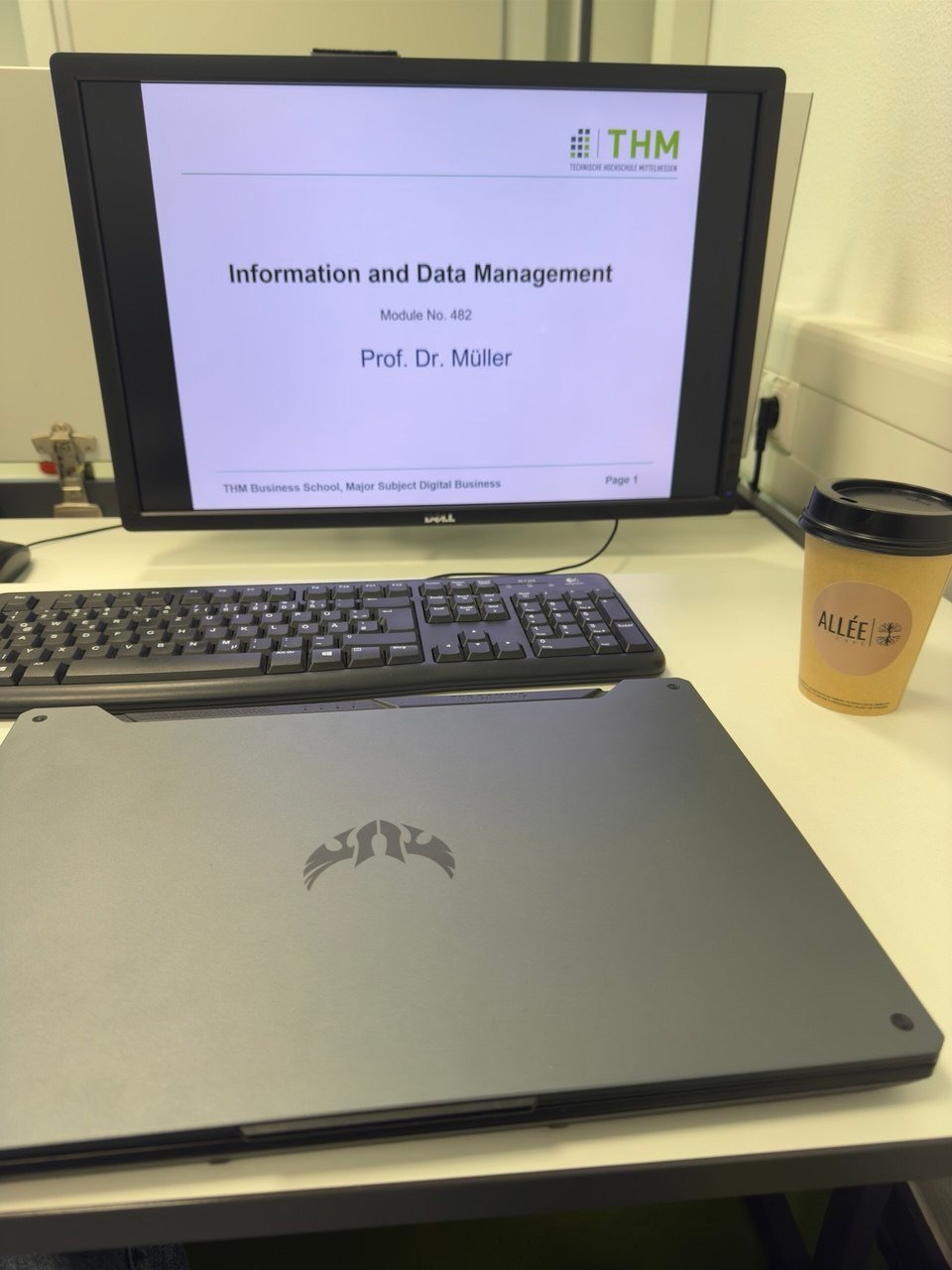 Слайд лекції «Information and Data Management» на моніторі, поруч клавіатура й ноутбук.